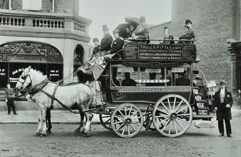 A double-decker omnibus approaching its full capacity, pulled by two horses down a city street.