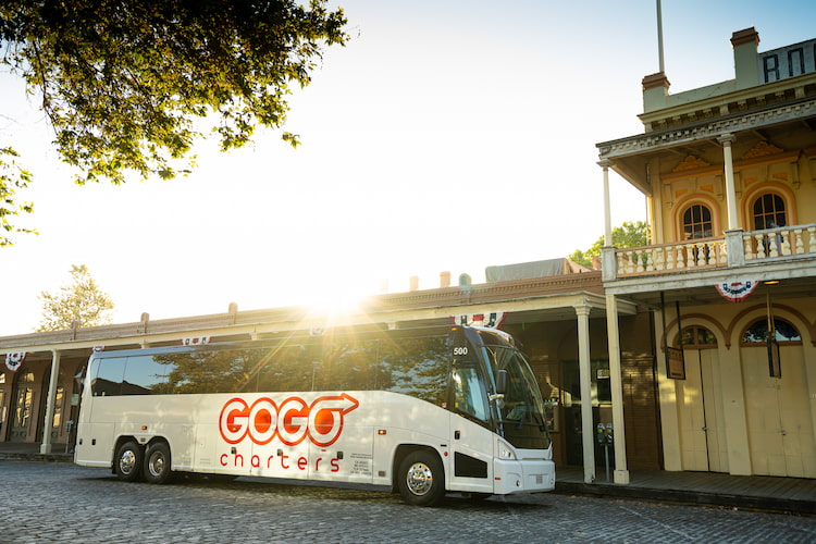 a plain white charter bus, with the "gogo charters" logo on the side, with the sun setting behind it