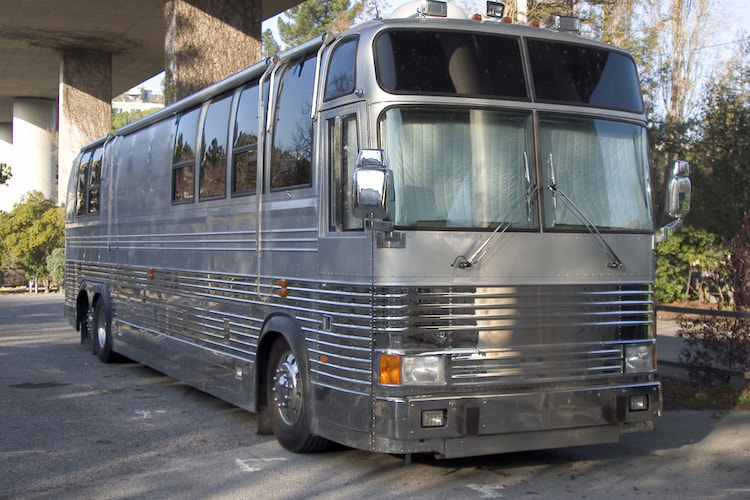 a metal gray tour bus exterior, parked under a freeway