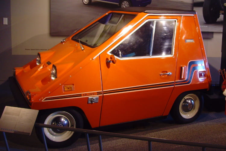 an orange 1976 Citicar sits in a car museum