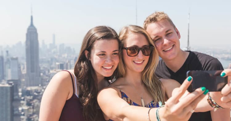 three tourists taking a photo in front of the new york city skyline