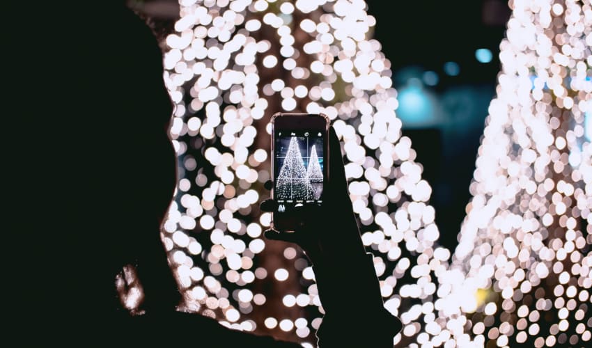 A woman takes a photo on her phone of a Christmas tree display full of lights