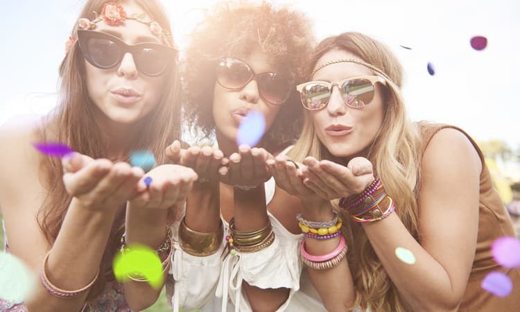 three women blow confetti around at a festival