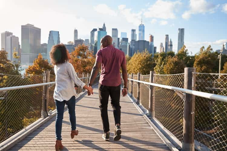 couple hold hands as they walk on nature trail towards manhattan, new york city