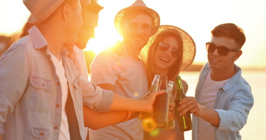 a group of friends toast bottles of beer on the beach