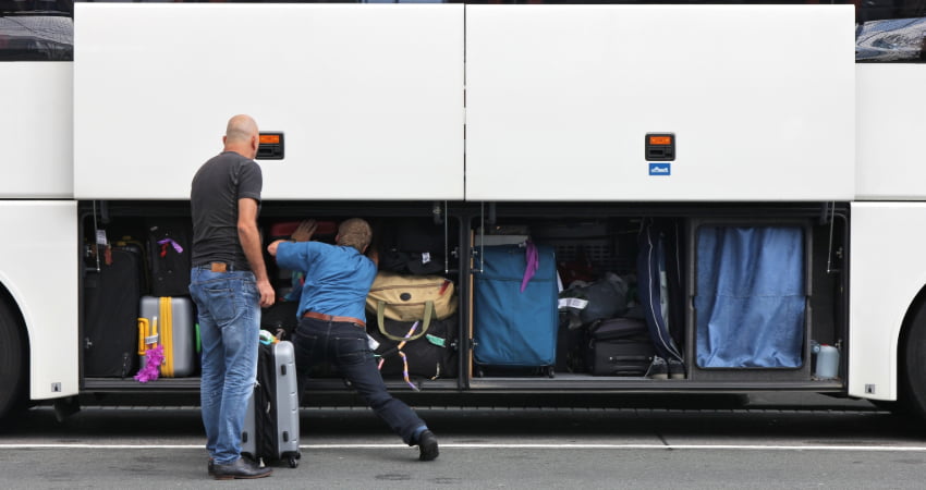 two men load luggage into a storage bay of a charter bus