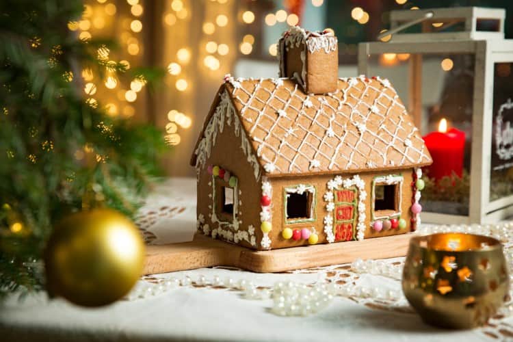 A holiday gingerbread house near a Christmas tree.