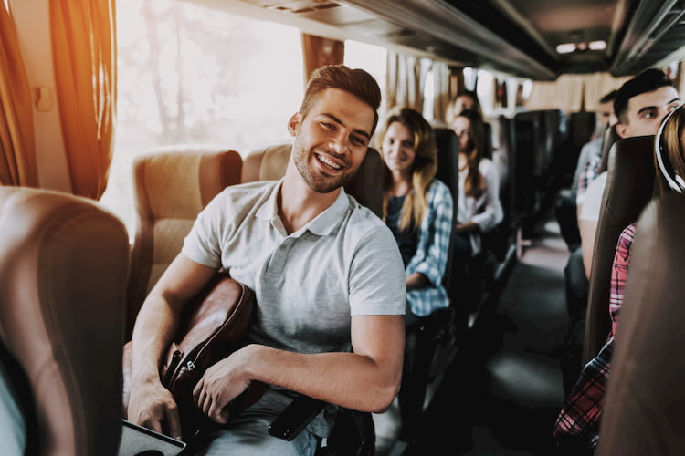 Attractive Smiling Man Sitting on Passenger Seat of Tourist Bus and Holding Backpack