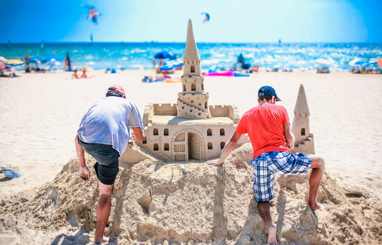 Two adult men build a sand castle on the beach