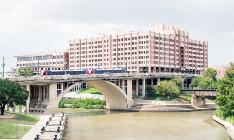 view across the river of a train passing in front of a University of Houston building