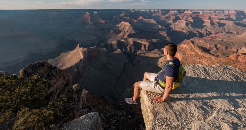 a tourist sits on the rim of the Gran Canyon and watches the sun set