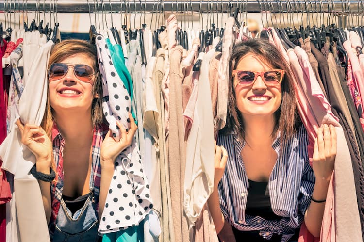 Best friends shopping in clothing rack on sunny day.