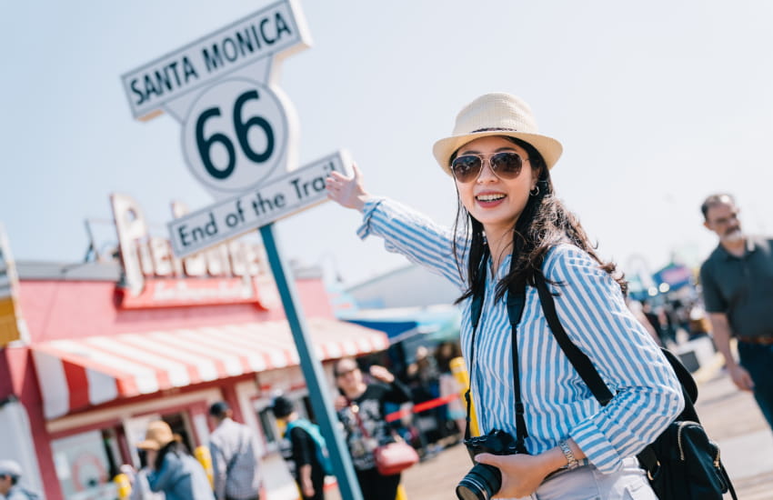 a woman with a camera poses for a photo by the Route 66 sign in Santa Monica