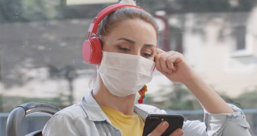 A woman wearing a mask and headphones on a bus