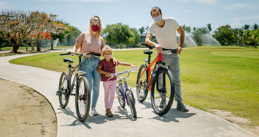 a family of three ride bikes on. paved trail while wearing masks