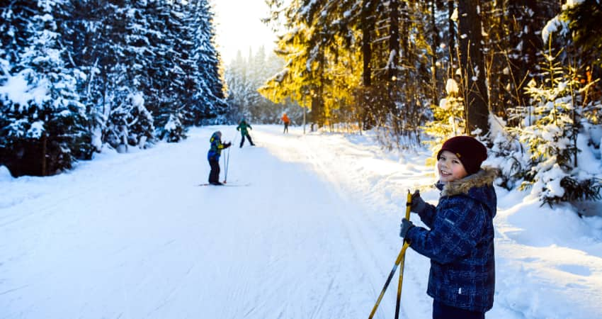 A child and his friends ski along a tree-lined trail