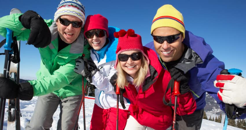 two couples stand and pose for a photo on a snowy peak with skis ready