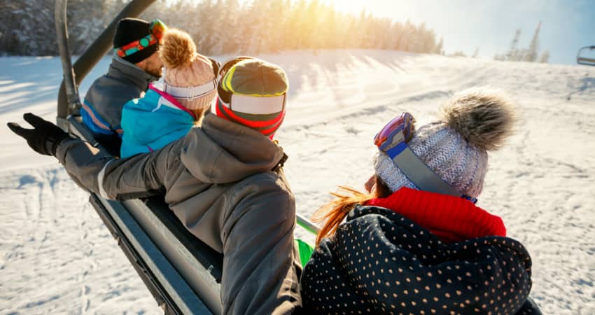 four skiers sit on a ski lift as it carries them to a snowy peak