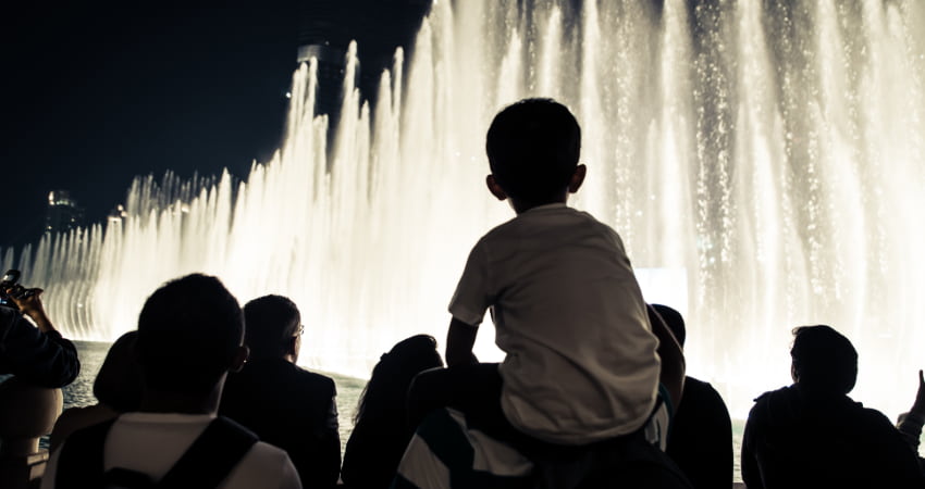 A child sits on their parent's shoulders as they watch the Bellagio Fountain show at night