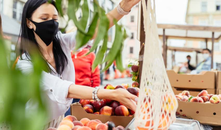 A woman wearing a mask and shopping for fruit at a farmers market