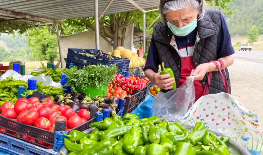 A woman wearing a mask weighs peppers on a scale in a farmers market