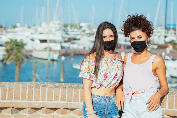 Two women wearing masks in front of ocean