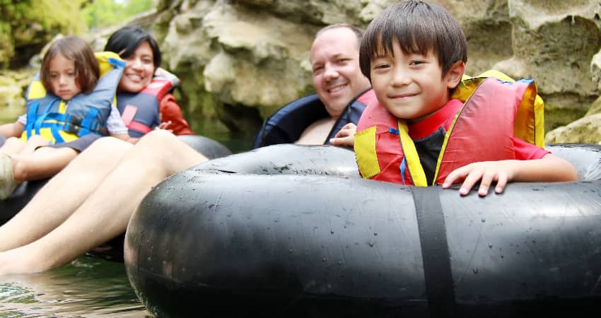 A family with two kids sit in inner tubes on a river, smiling