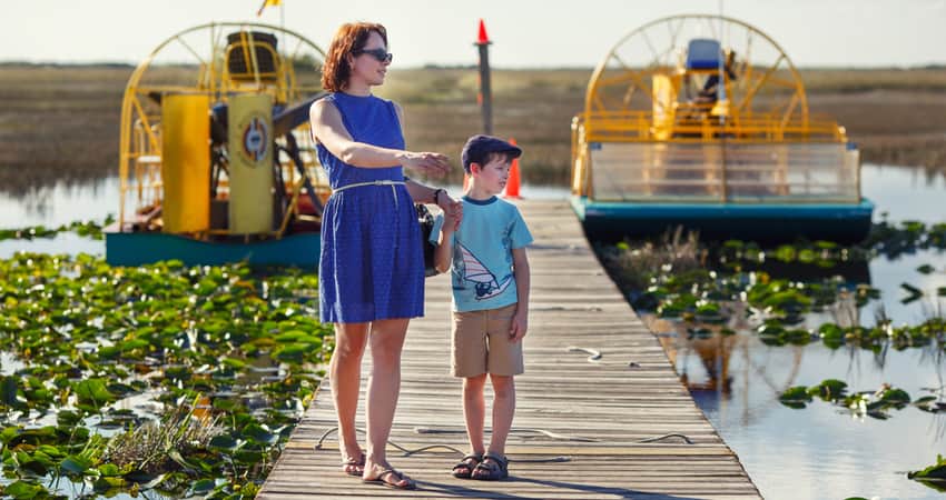 A woman and child on an Everglades boardwalk with air boats in the background 