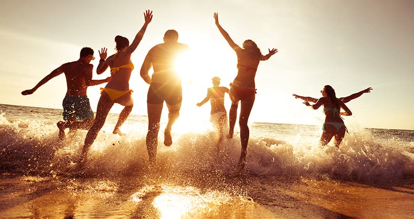 A group of adults run into the ocean on a sunny beach
