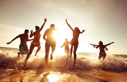 A group of adults run into the ocean on a sunny beach