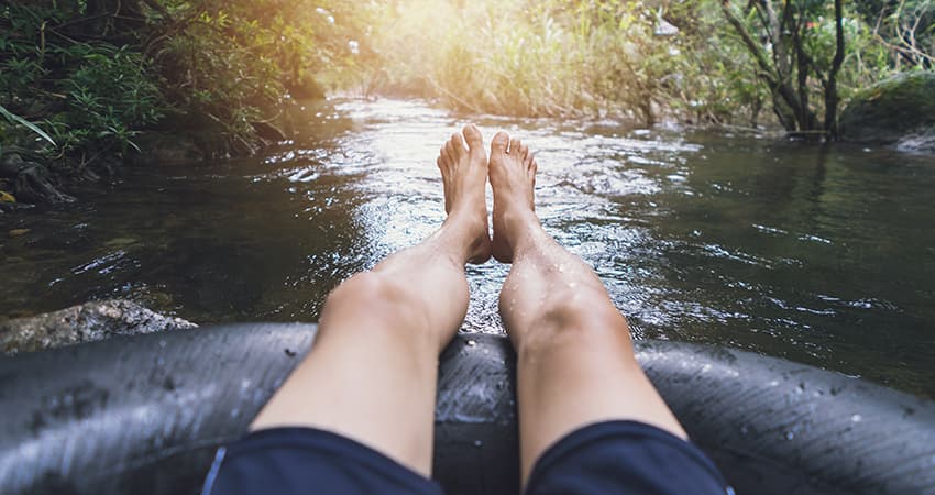 A person with bare feet sits in a tube floating along a river