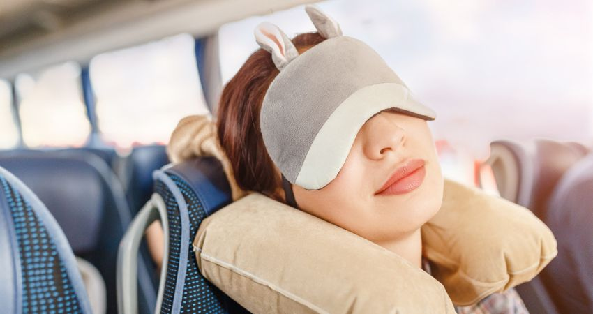Smiling woman comfortably sleeping on a charter bus with an eye mask and neck pillow.