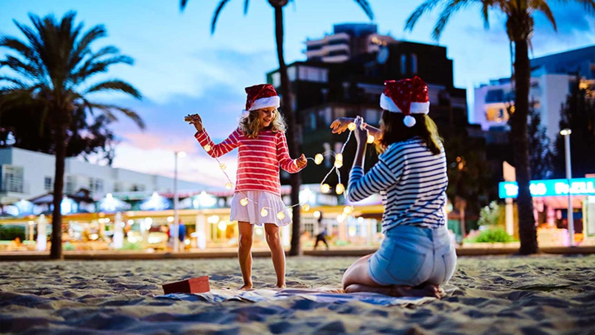Girl and woman in Santa hats playing with lights on a beach