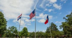 A French flag, Texas flag, and USA flag flying side by side.