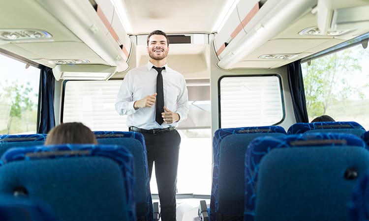 A tour guide smiles and talks to a crowd aboard a charter bus