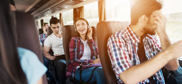 a woman with headphones on smiles while she sits in a comfortable charter bus seat next to a large window