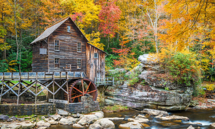 an old mill over a river in west virginia, surrounded by red and gold leaves