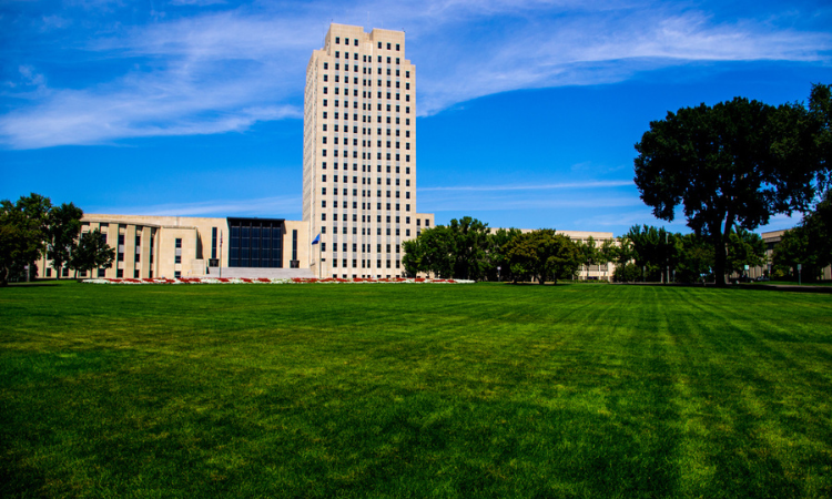 a lush green field with a tall north dakota office building in the background