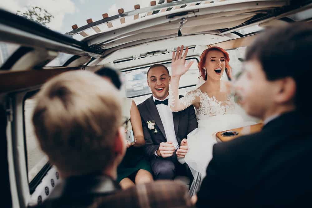 Red-haired bride and dark-haired groom in back of limo with friends