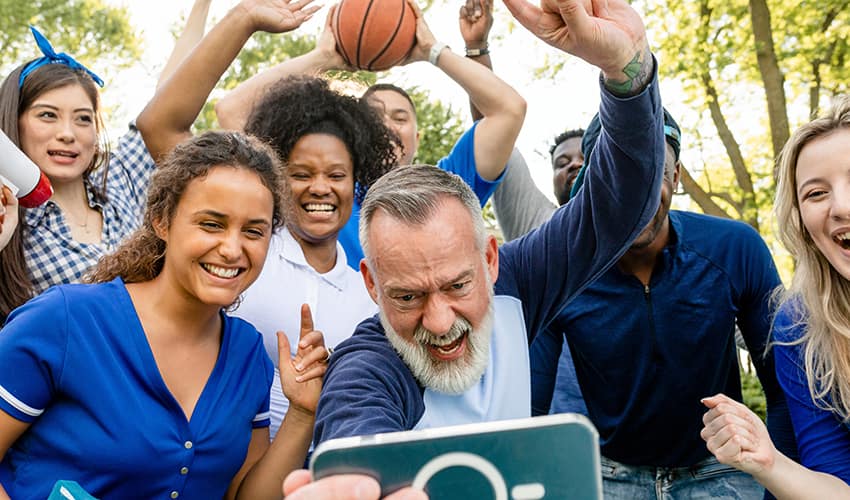 A group of basketball fans in blue clothes gather around a phone, cheering