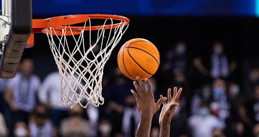 A basketball player tips a basketball into a hoop in a stadium