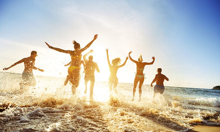 A group of young adults jump into the waves on a sunny beach