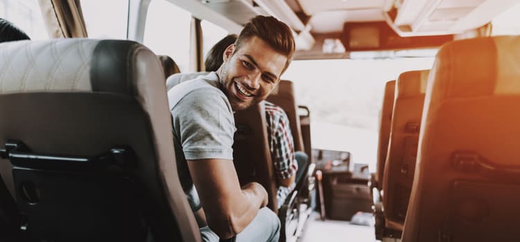 a man turns around in his bus seat and smiles at someone behind him