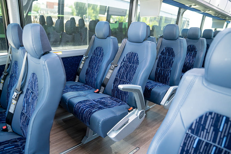 Charter bus seats with seatbelts and a faux-wood interior.