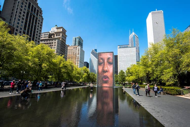 a screen with a woman's face over a reflecting pool at millennium park