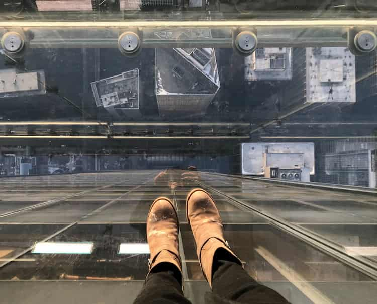 a view of a guest's feet as they stand atop Willis Tower and look toward the street