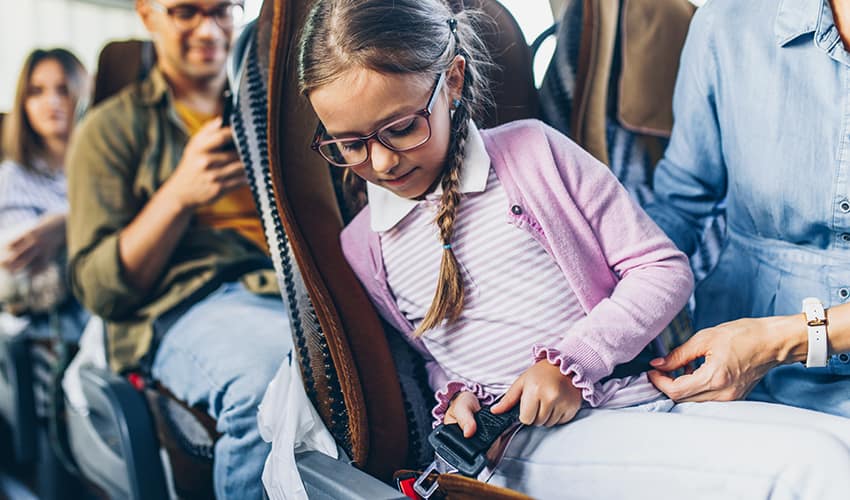 A little girl buckles the seatbelt on her seat in a charter bus