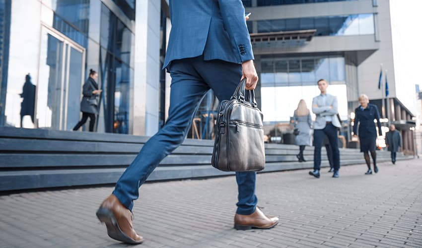 A professional in a suit holds a briefcase and walks toward an office building