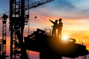 silhouette of two construction site workers on a crane