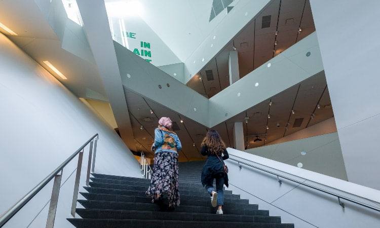 two women walk up the stairs in the main atrium of the denver art museum